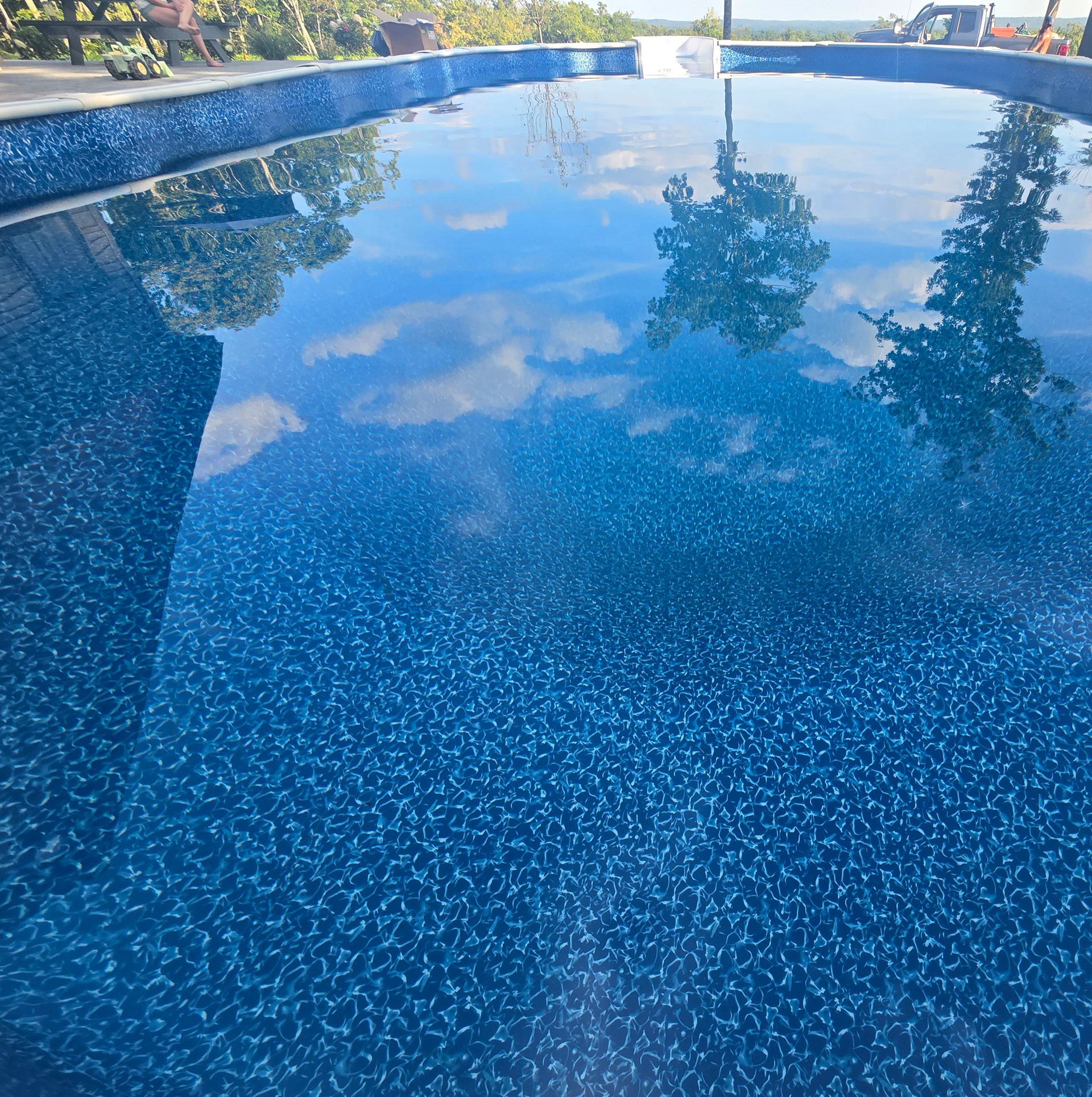 A blue swimming pool with trees reflected in the water