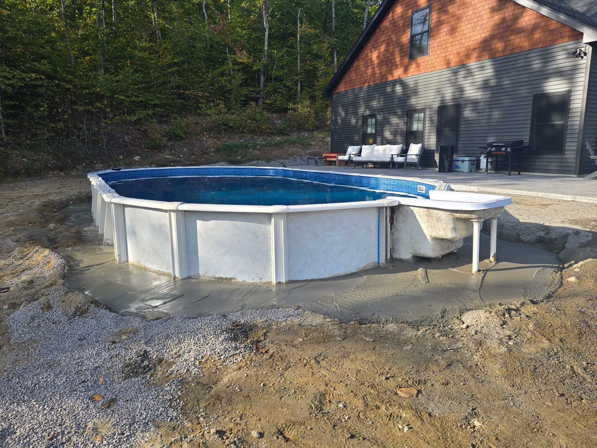 A large swimming pool is sitting in the dirt in front of a house.