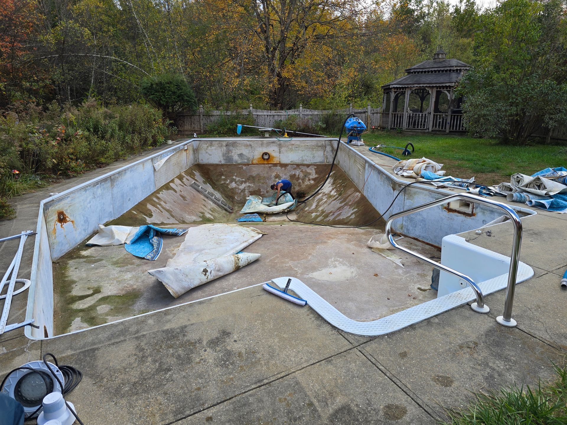 An empty swimming pool in a backyard with a gazebo in the background.