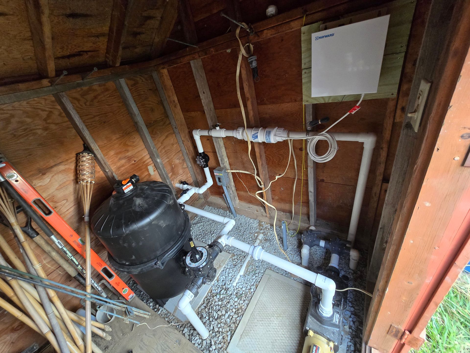 A shed with a pool pump and pipes in it.