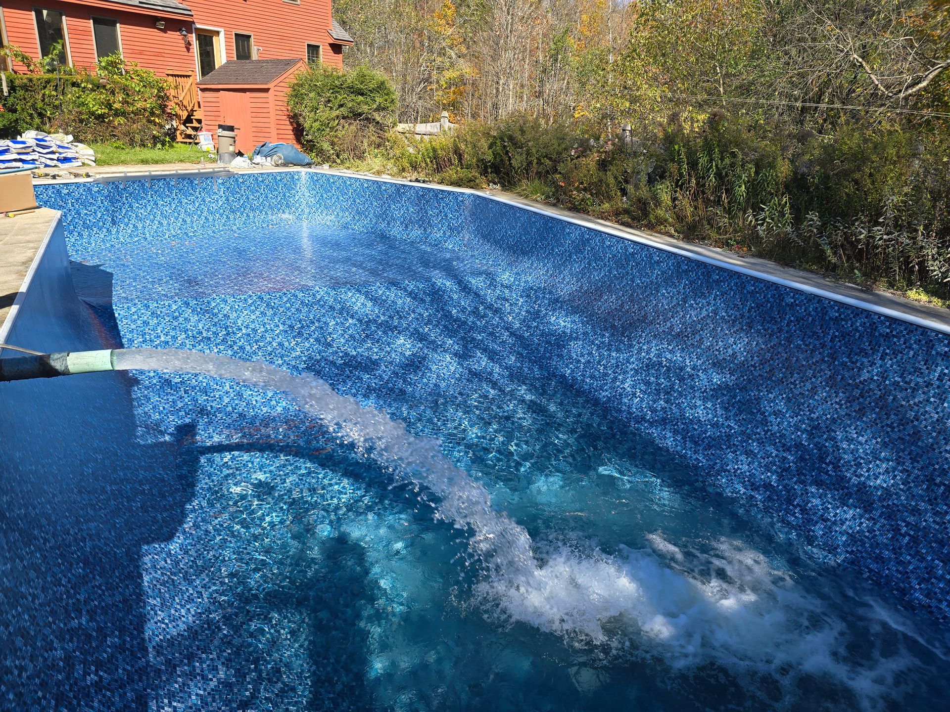 A person is pumping water into a swimming pool with a hose.