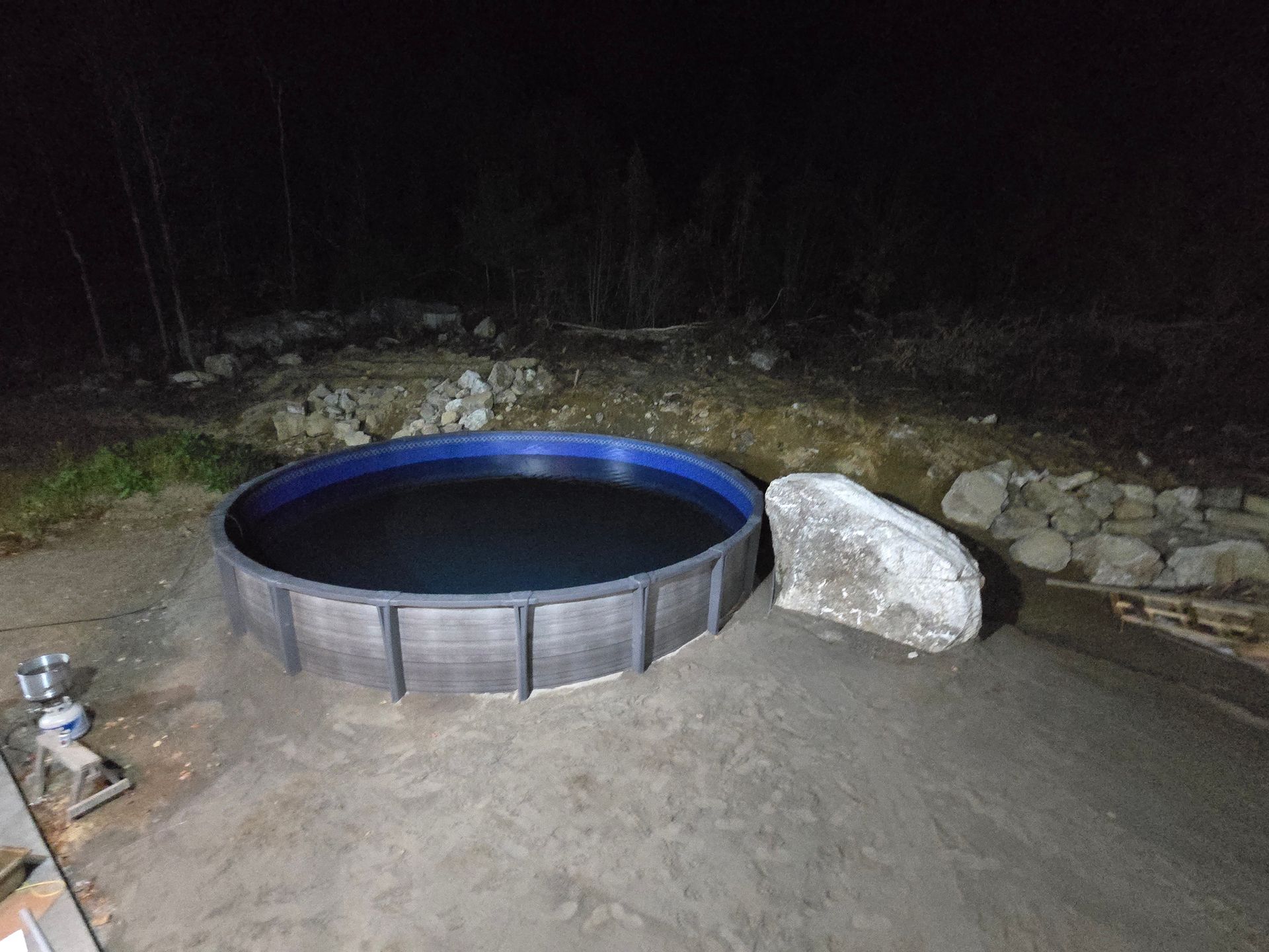 A large swimming pool is sitting on top of a dirt field at night.