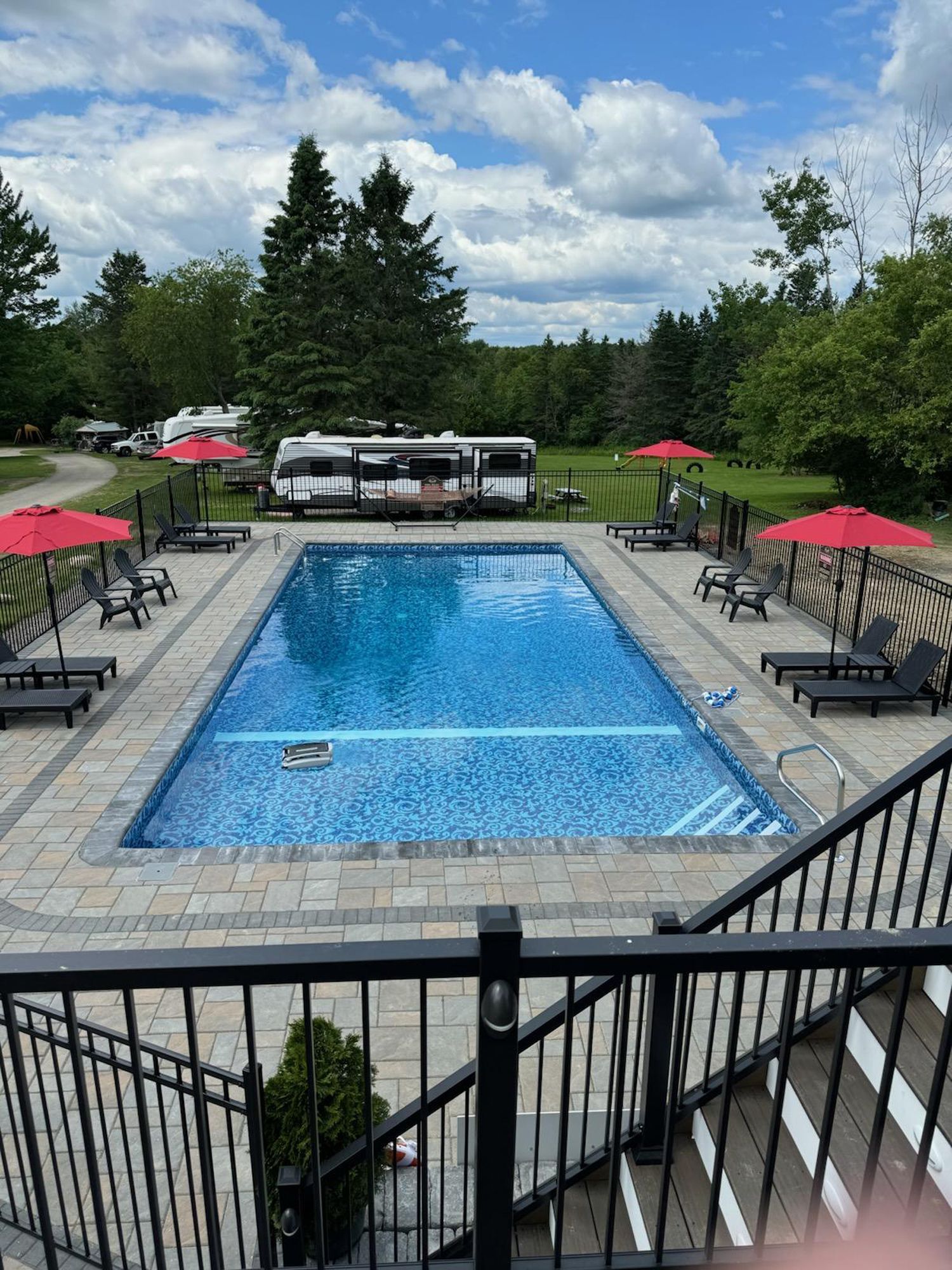 A large swimming pool surrounded by chairs and umbrellas with a rv parked in the background.