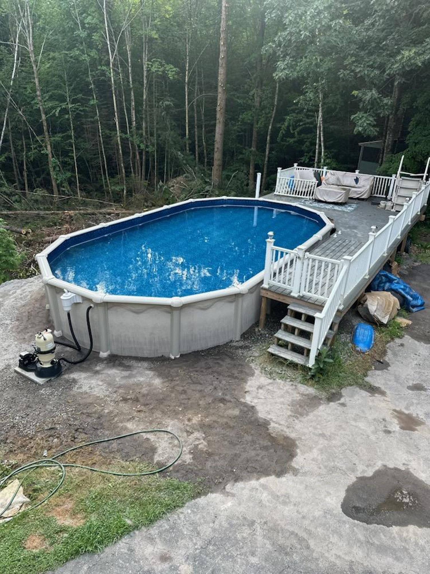 An oval swimming pool with a deck and stairs in a backyard.
