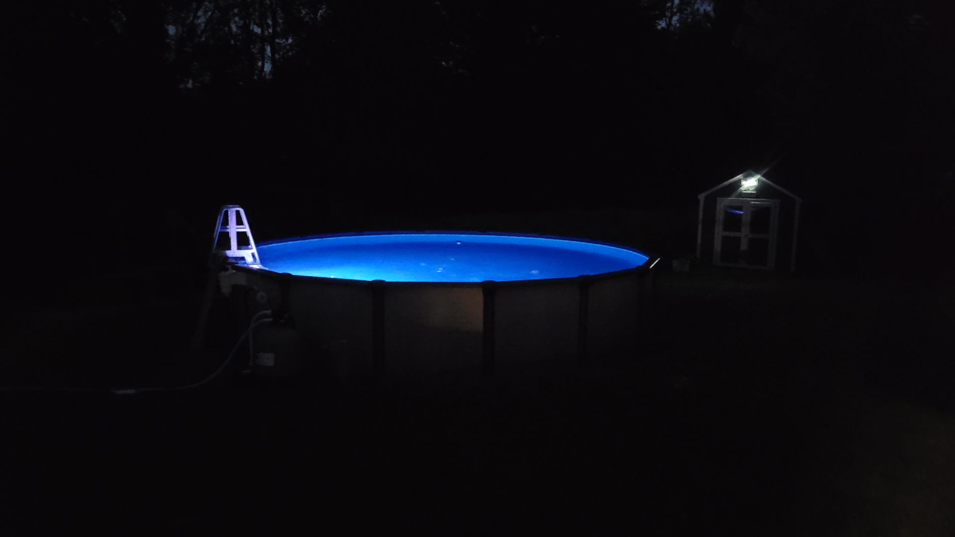 A swimming pool is lit up at night with blue lights.
