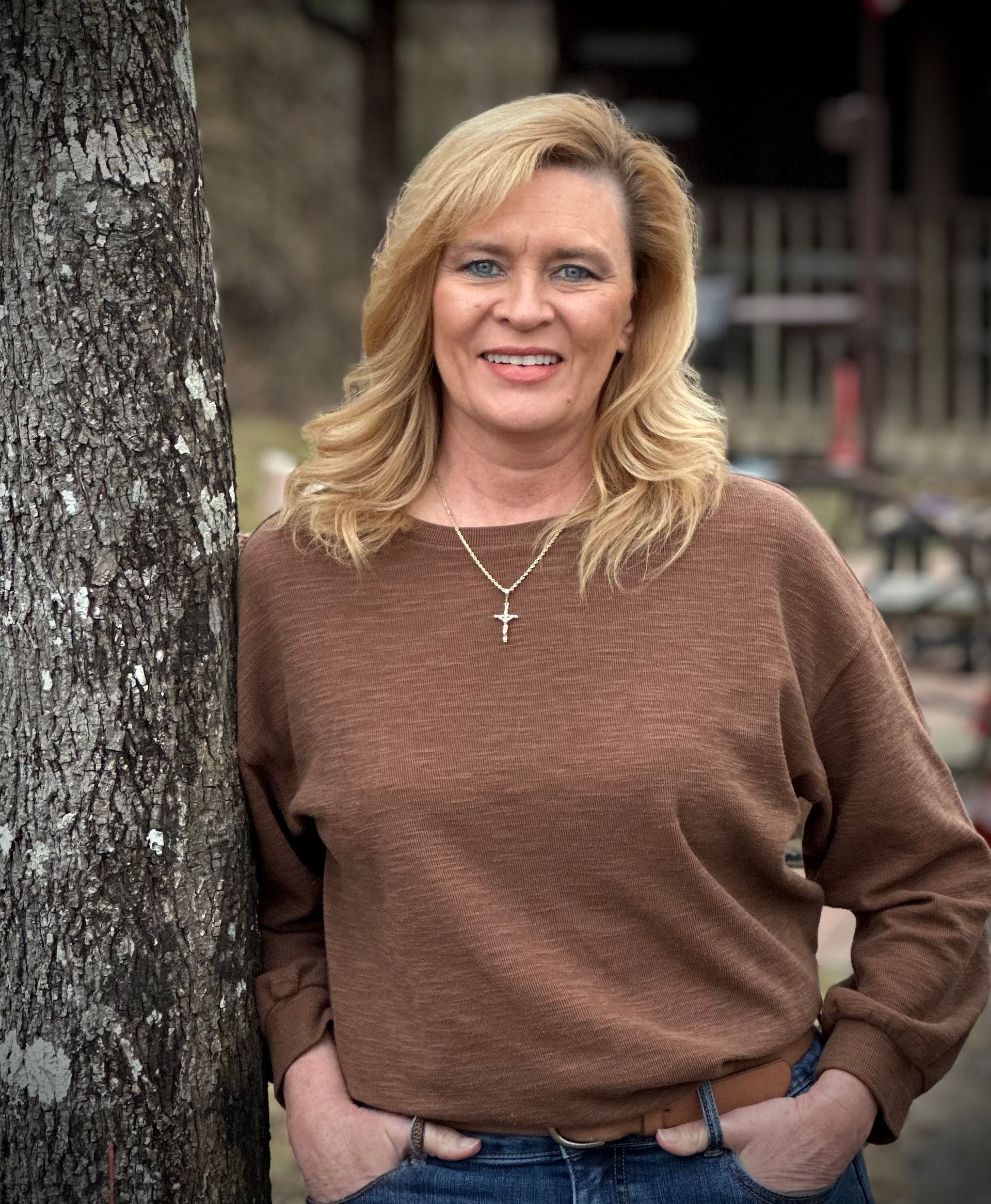 A woman is sitting at a desk with a laptop and a vase of flowers.