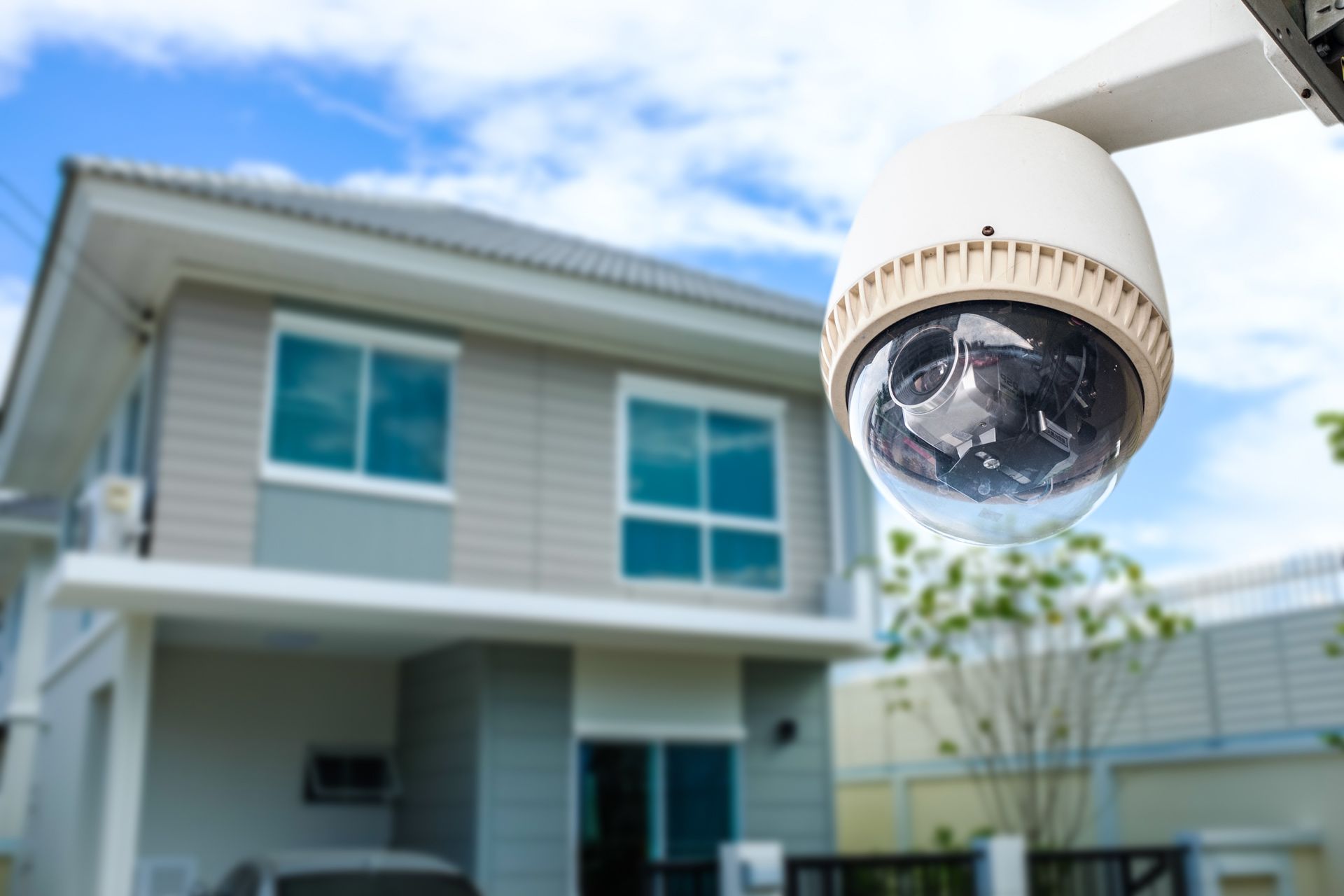 A security camera is hanging from a pole in front of a house