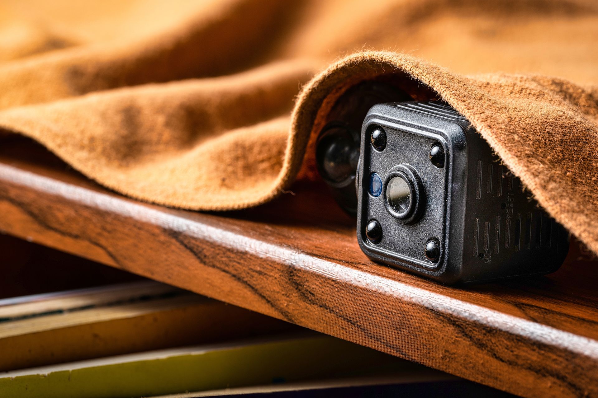 Black camera peeking from under a tan leather sheet on a wooden surface.