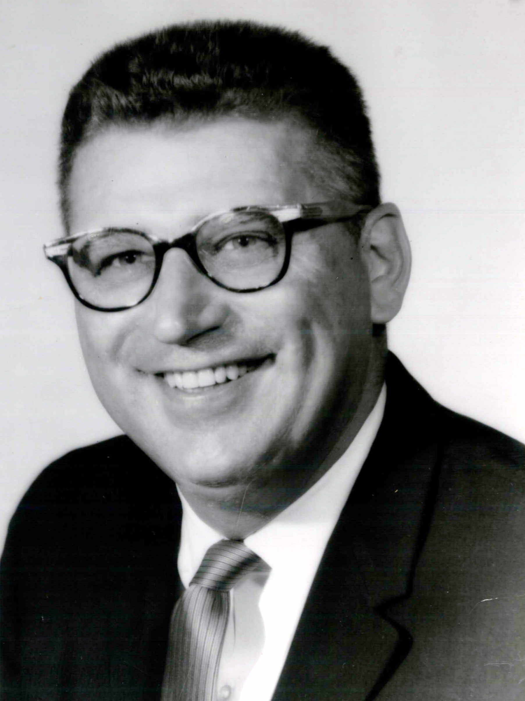 A man wearing glasses and a suit smiles for the camera