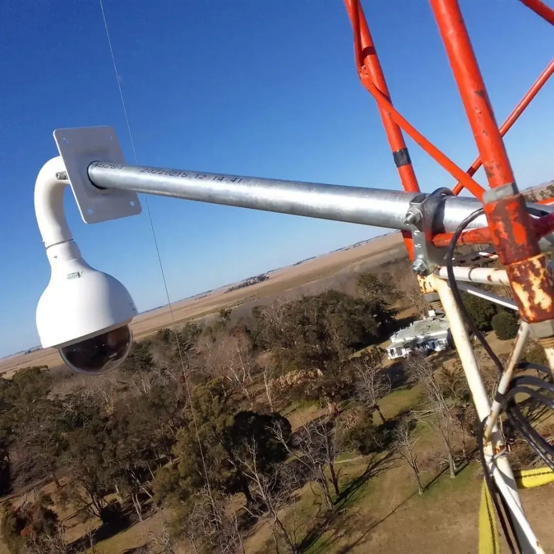 Cámara de seguridad instalada en una torre roja y plateada, con vistas a un paisaje.