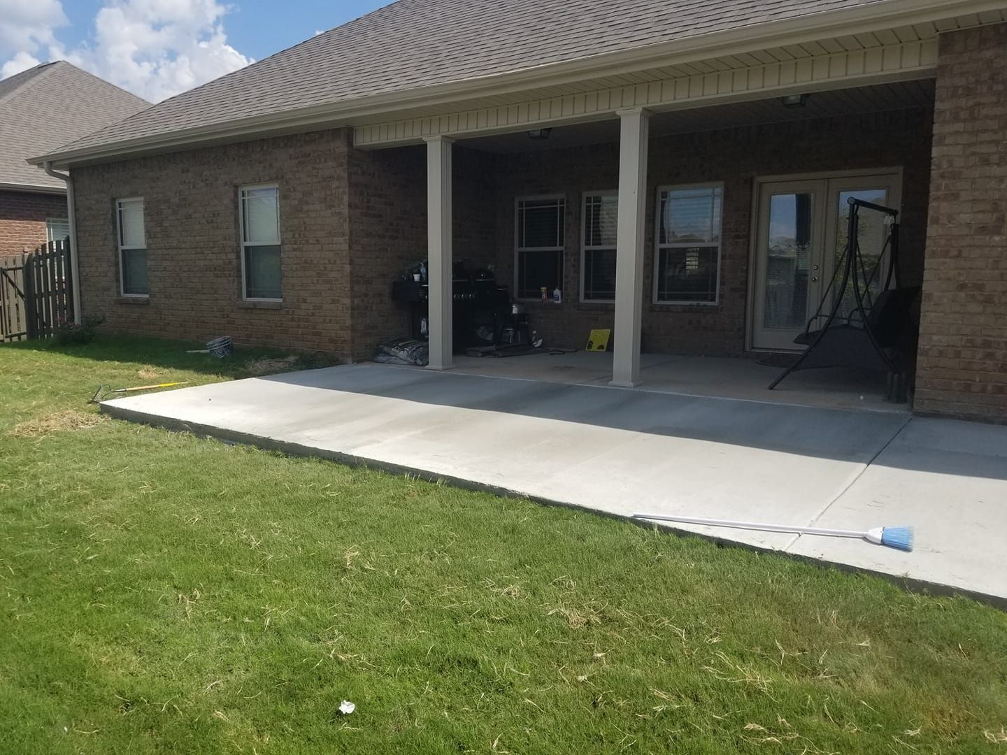 A brick house with a concrete patio and green lawn. Patio is covered, open to the yard.