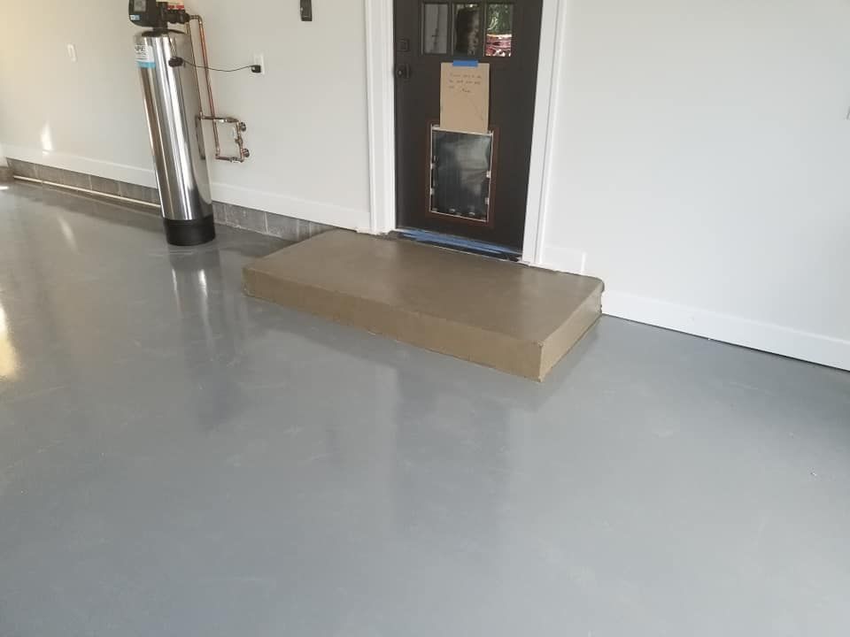 A shiny, gray garage floor with a brown box and a metallic water filter by a dark door.