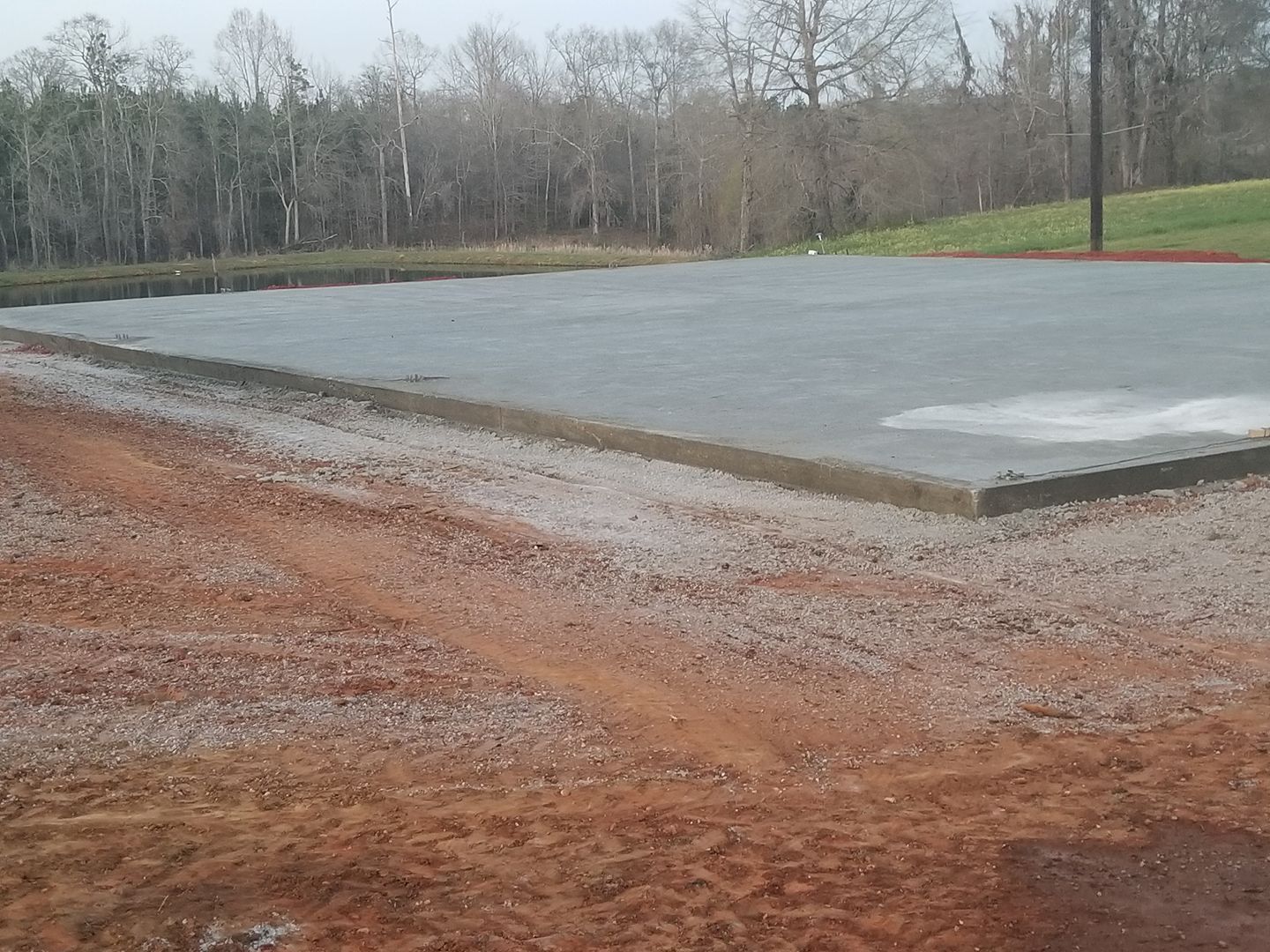 Newly poured concrete slab on a gravel bed, with trees in the background.