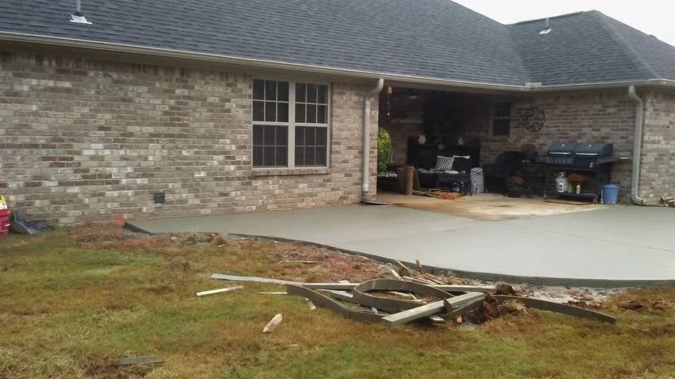 Newly poured concrete patio next to a brick house, partially on a grassy lawn.