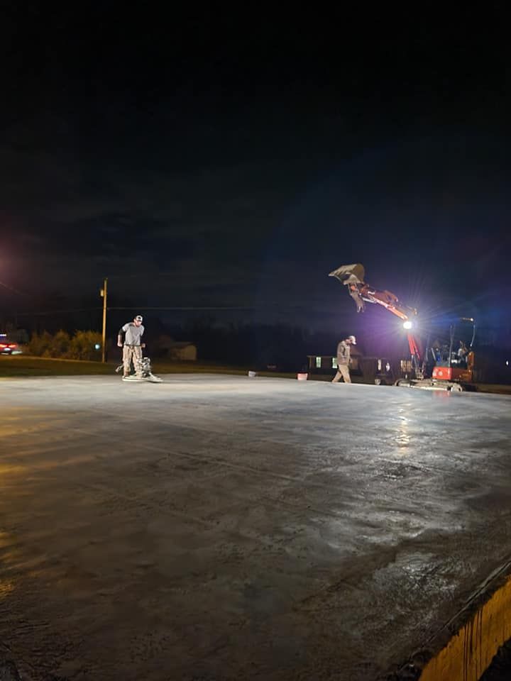 Construction workers smoothing concrete at night using equipment under bright lights.