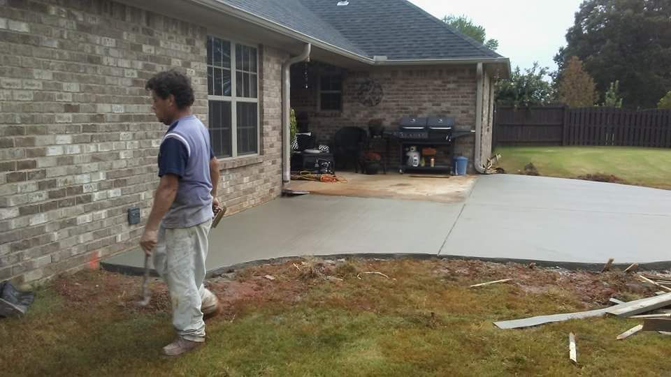 Man standing near newly poured concrete patio next to a brick house.