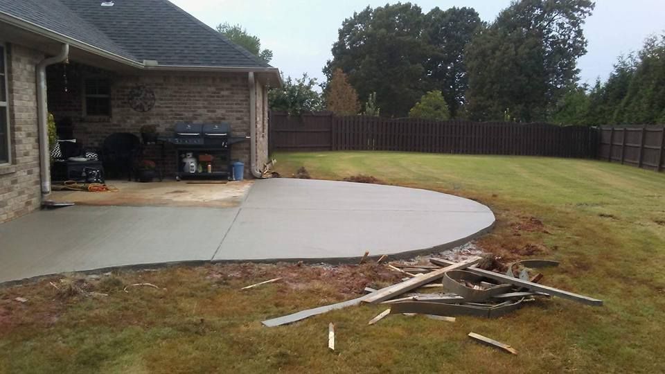 Newly poured concrete patio next to a brick house and grassy backyard. Wood debris in foreground.