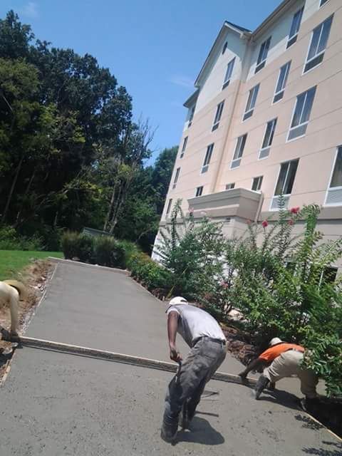 Workers smoothing fresh concrete sidewalk beside a multi-story building on a sunny day.
