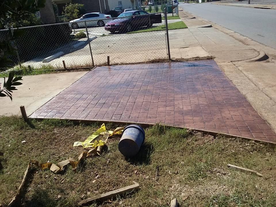 Brown stamped concrete driveway with a bucket and debris on the grass.