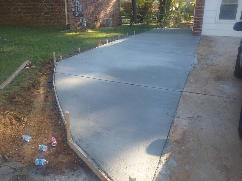 Newly poured concrete driveway with wooden forms, beside a house and yard.