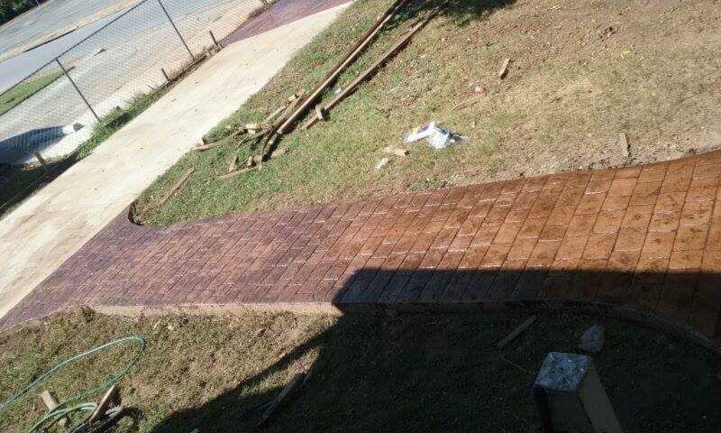 Brown stamped concrete walkway curving from a concrete path on grass.