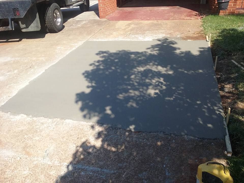 Freshly poured concrete slab next to a driveway and lawn; shadow of tree is cast on the new concrete.