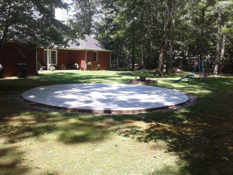 Circular concrete patio in a backyard, surrounded by grass and trees, with a house in the background.