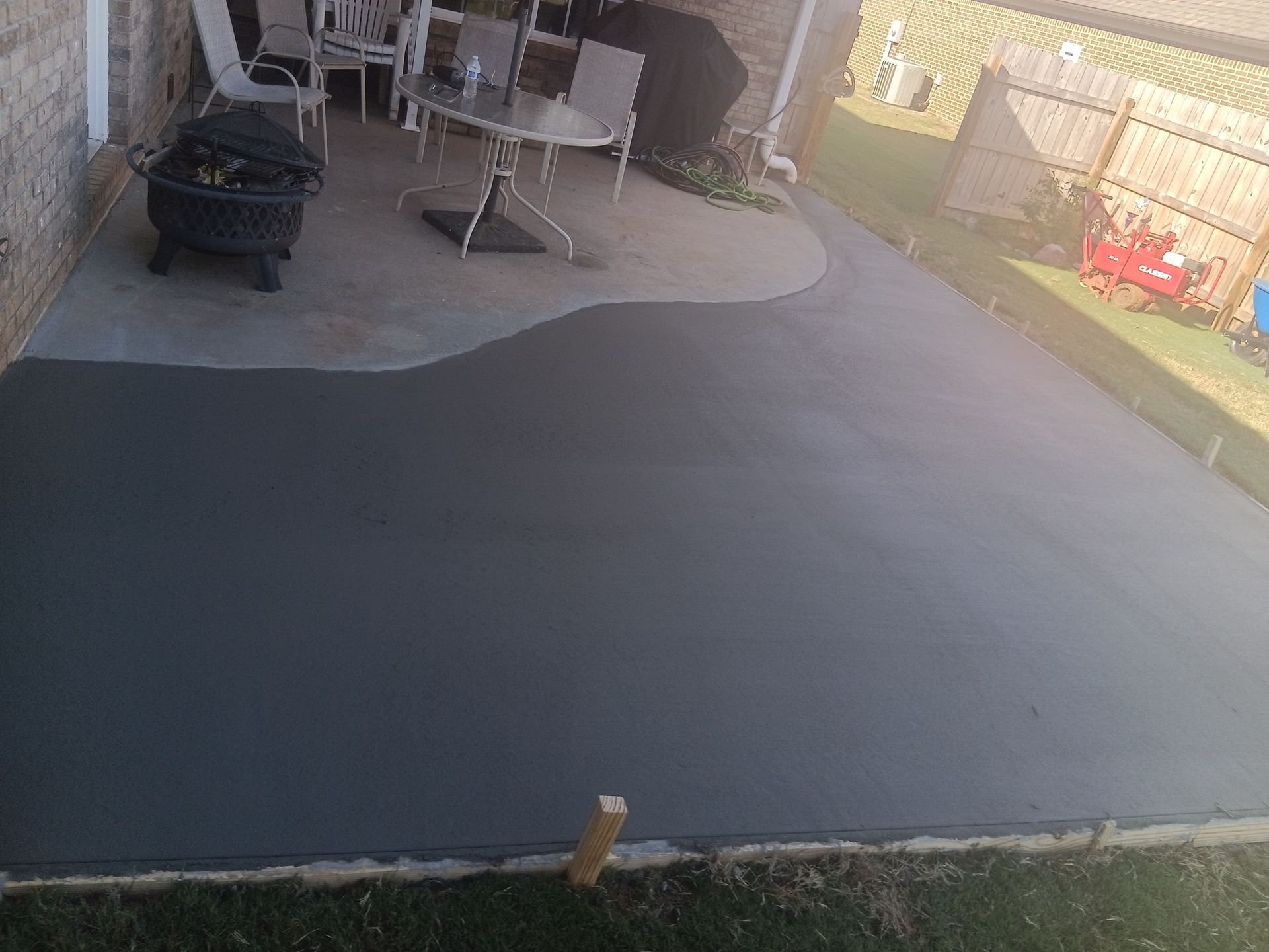 Concrete patio with a darker gray section. Furniture and fire pit visible.