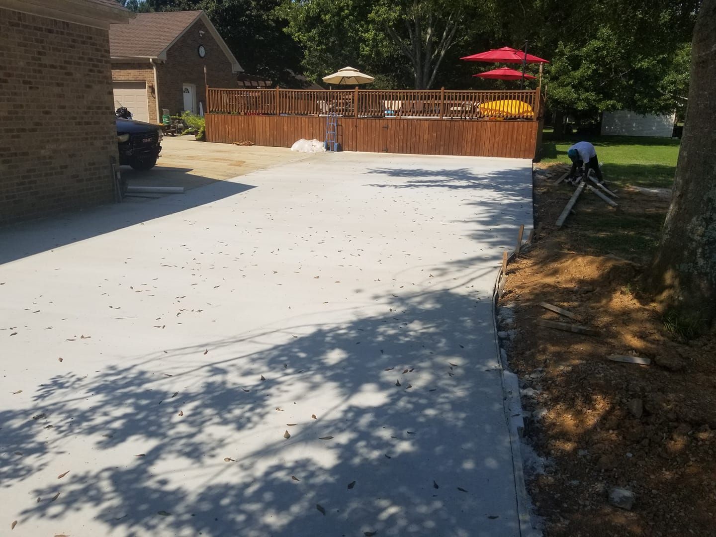 Newly poured concrete driveway leading to a wooden deck, person surveying, sunny outdoor setting.