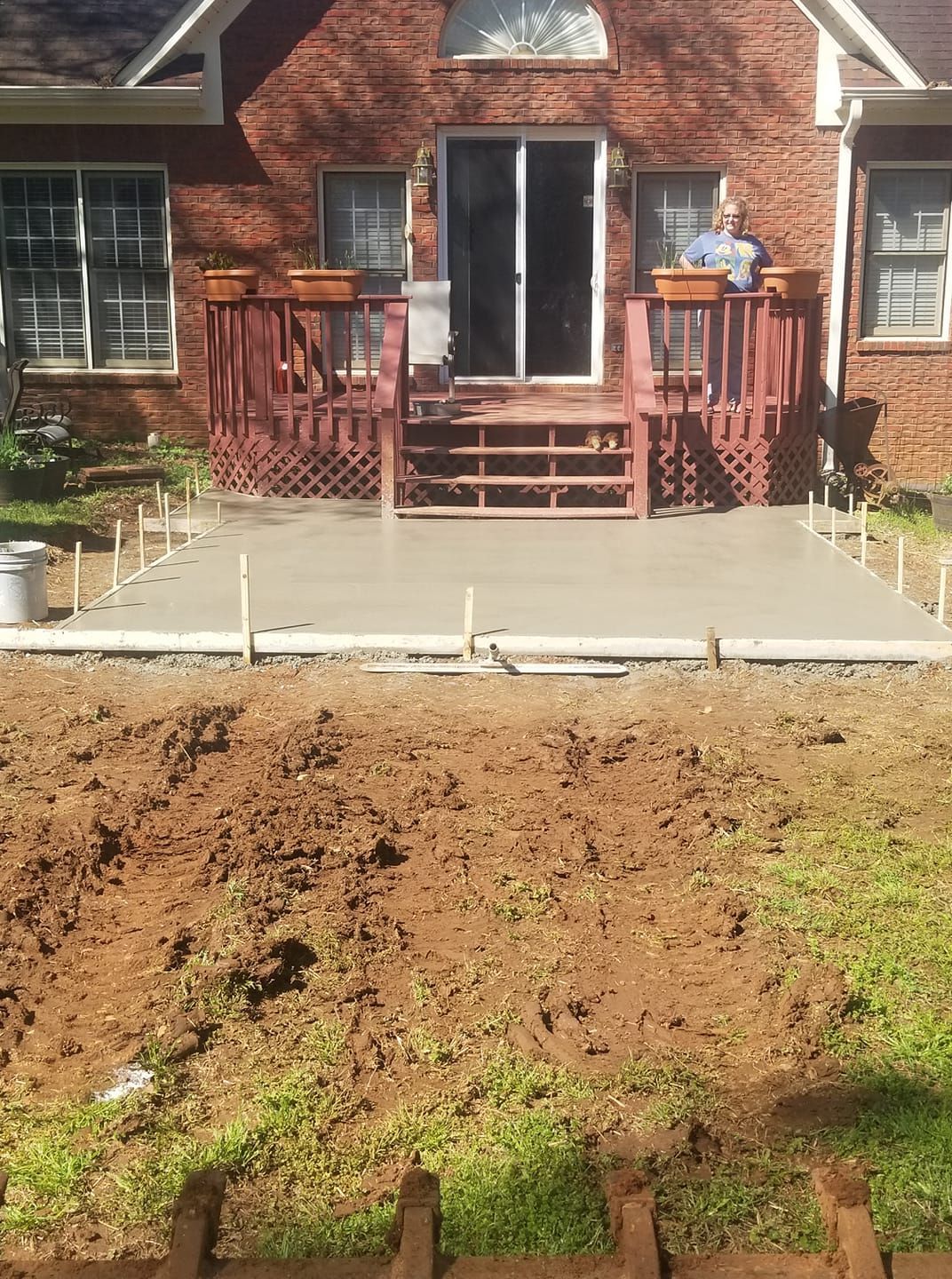 Newly poured concrete patio in front of a raised deck with a brick house background.