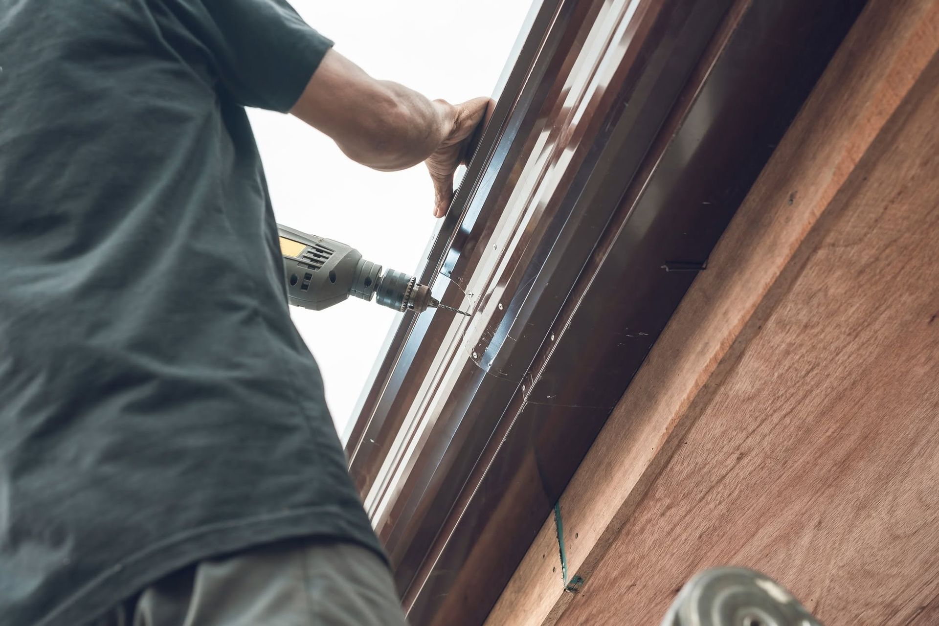 Person using a power drill to repair a brown roof edge from a ladder