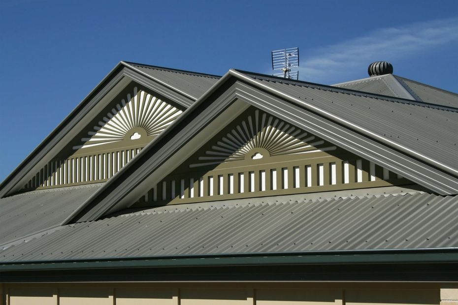 Gray metal roof with two triangular gables and sunburst vents against a blue sky