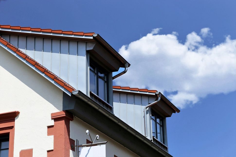 Red-roofed house with white walls and dormer windows against a blue sky with clouds