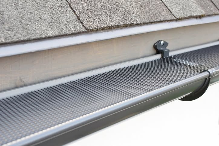 Gutter guard beneath roof shingles with a metal support bracket attached to the fascia
