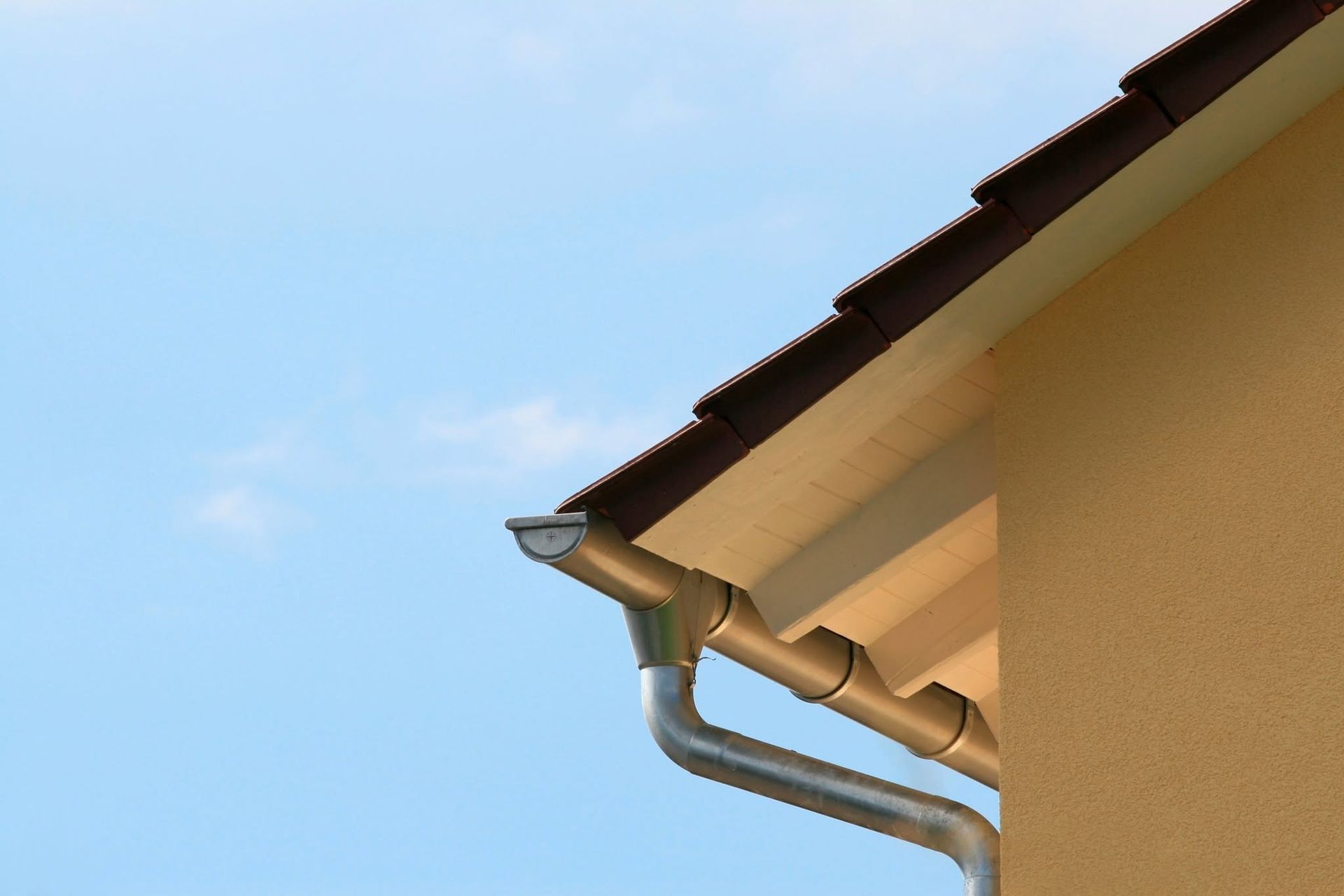 House roof corner with brown gutters and a downspout against a blue sky
