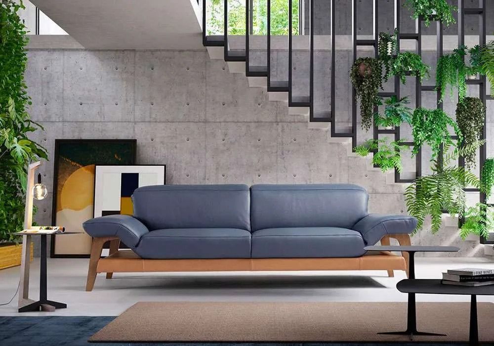 Divano in pelle blu in un soggiorno moderno con parete in cemento, piante e scale.