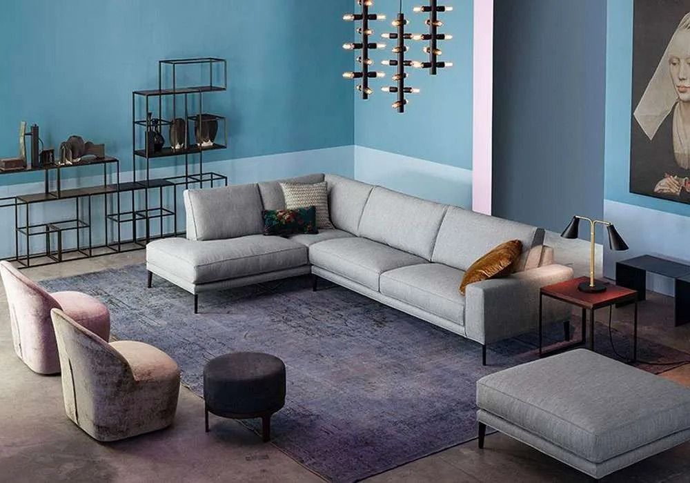 Soggiorno con divano componibile grigio, pareti blu, tappeto scuro, scaffali neri e opere d'arte.