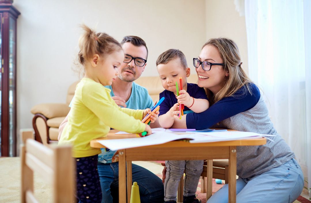 Family drawing together at a small table. Children, parents, and colorful markers.