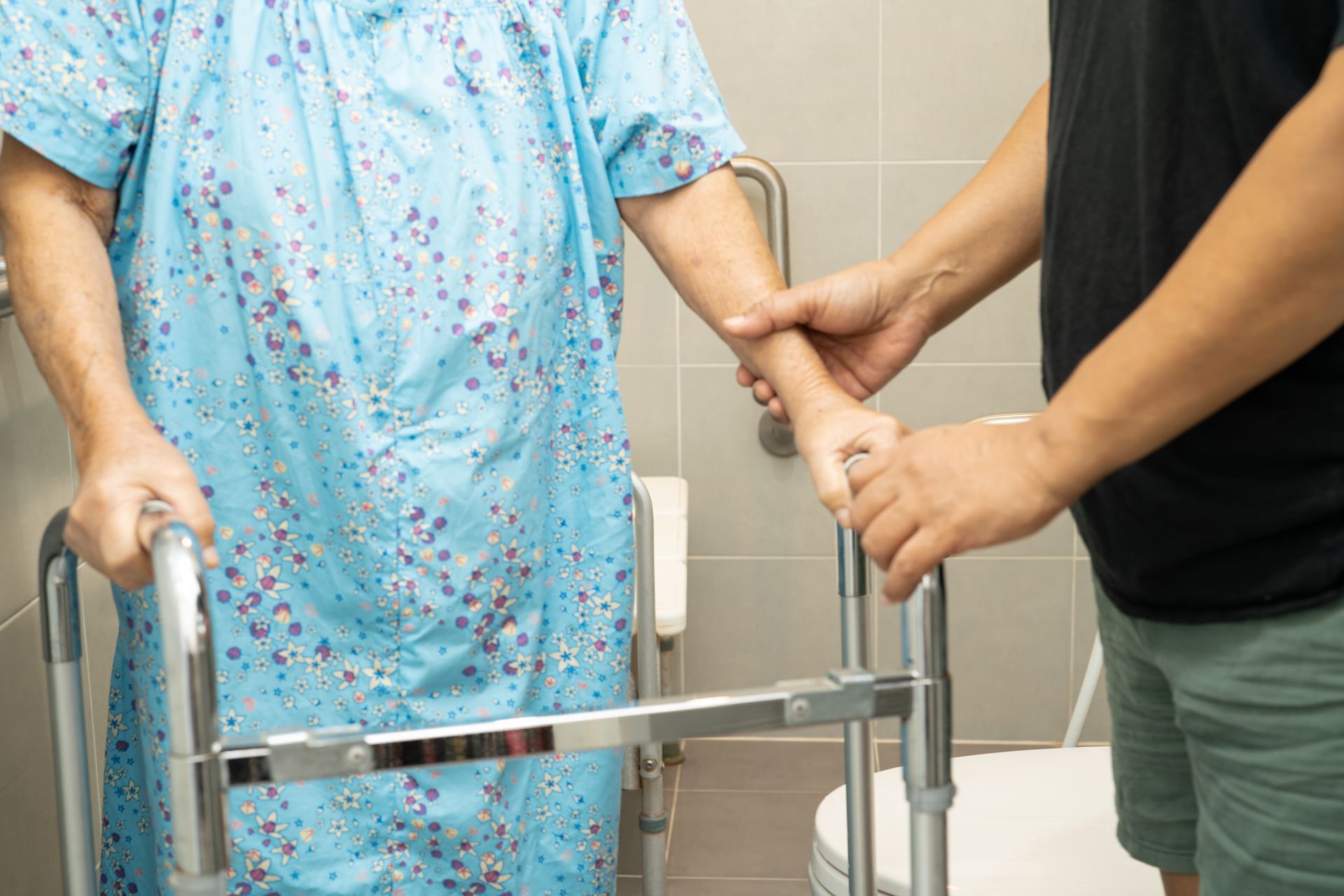 Caregiver help elderly woman patient use walker and toilet bathroom handle security.