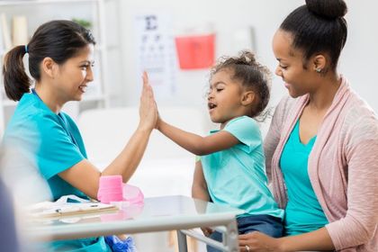 Doctor high-fives a young child in a medical office, child smiles while mother watches.