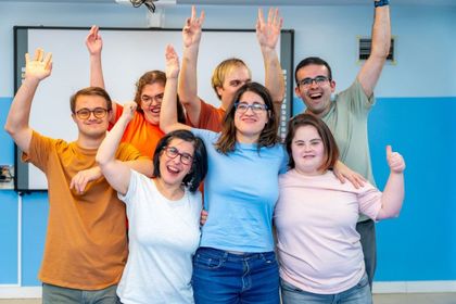 Group of people with raised arms, smiling in a room with blue walls, celebrating.