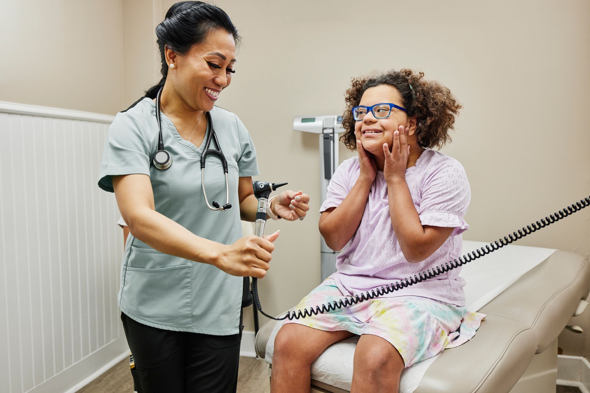 Medium shot of smiling nurse and young female patient with Down Syndrome in medical exam room during doctor visit.