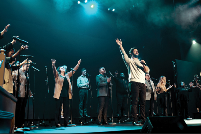 Five well-dressed men posing together in front of a dark background.