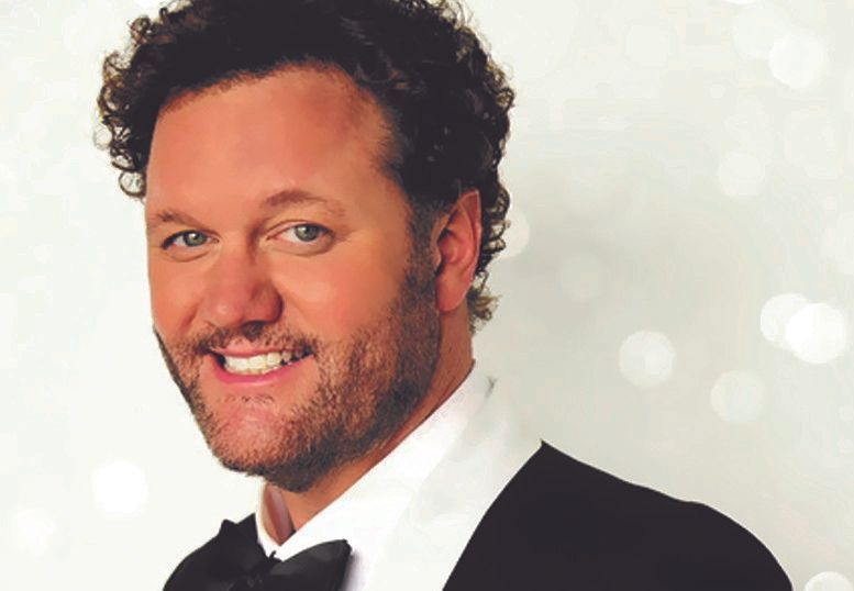 Man with curly brown hair, smiling. He's wearing a tuxedo with a black bow tie.