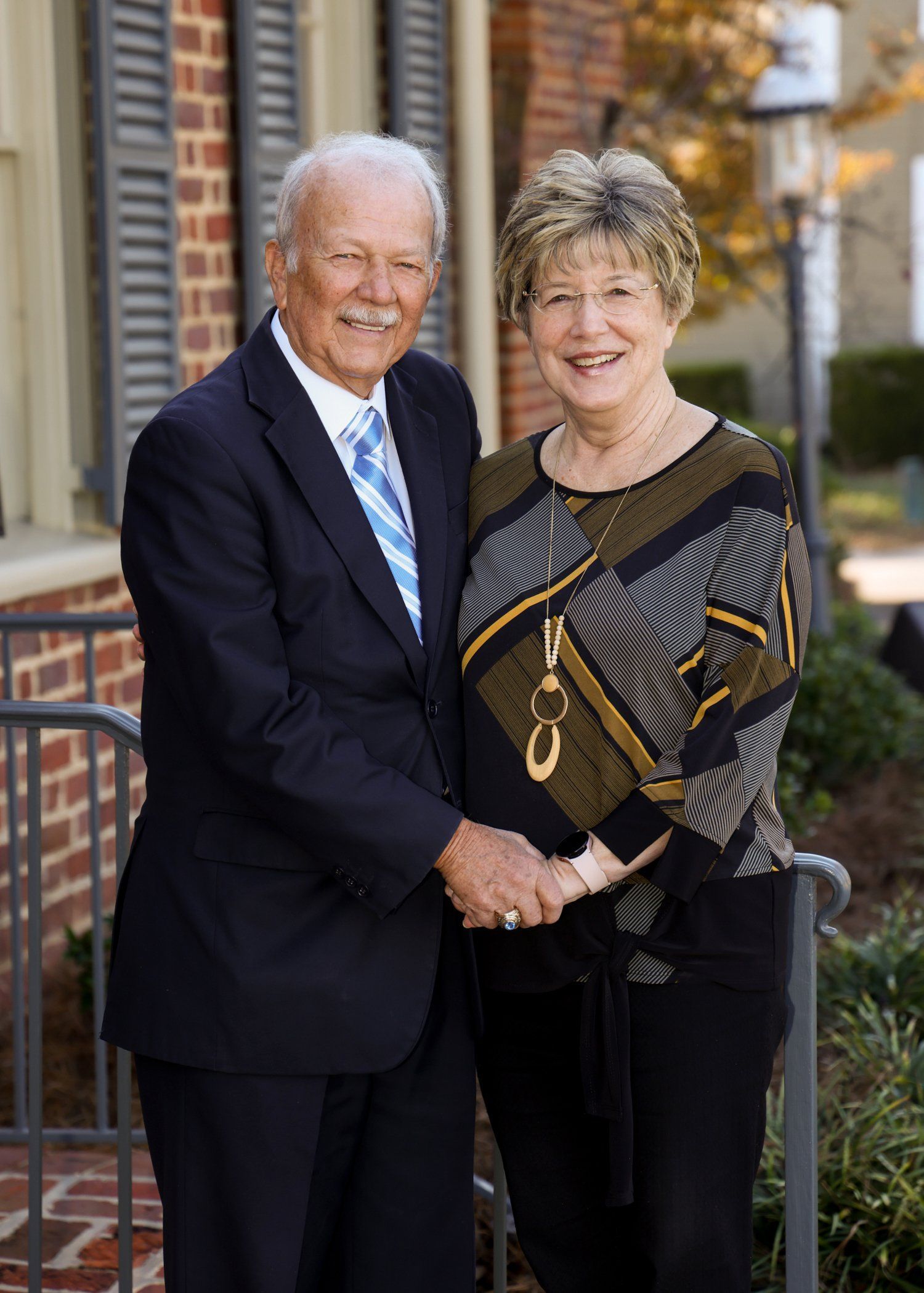 A man and a woman are shaking hands in front of a brick building.