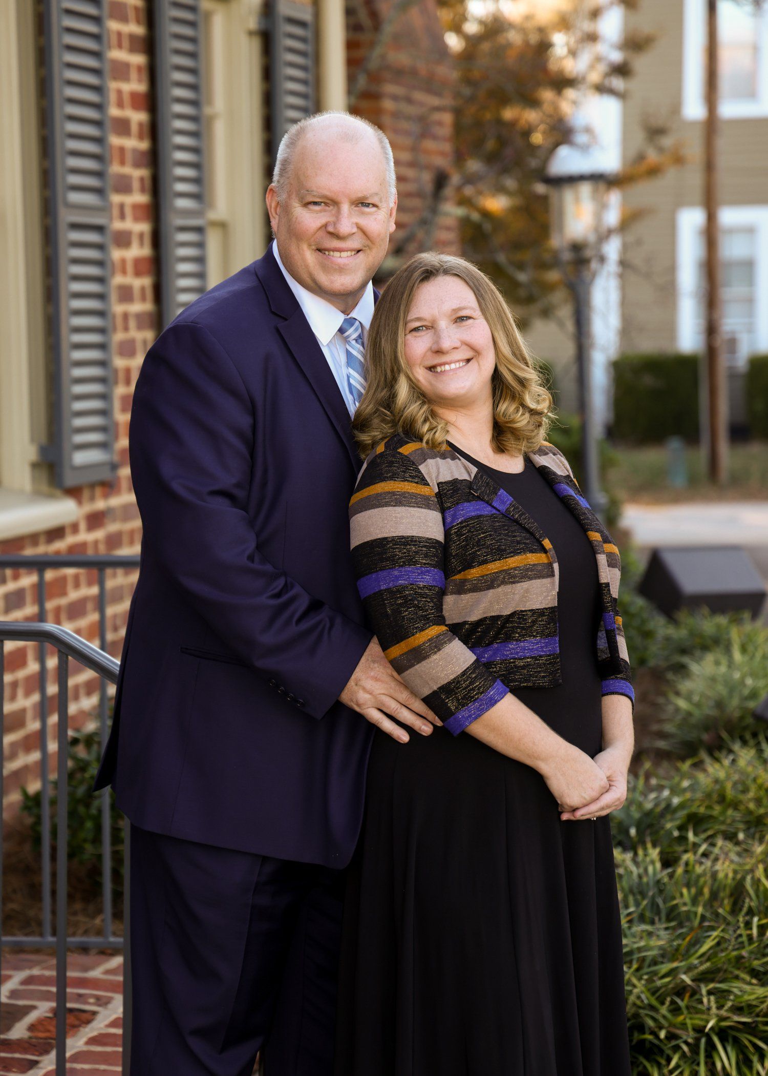 A man and a woman are posing for a picture in front of a brick building.