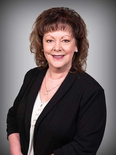 A woman in a black jacket and white shirt is smiling for the camera.
