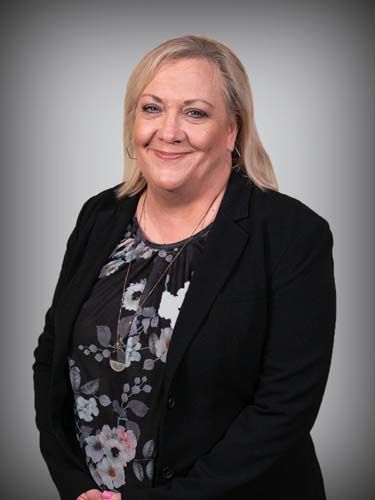 A woman in a black jacket and floral shirt is smiling for the camera.