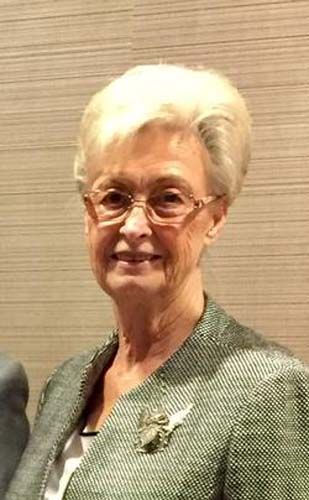 A woman wearing glasses and a green jacket is smiling for the camera.