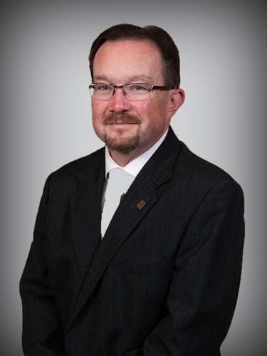 A man with glasses and a beard is wearing a suit and tie.